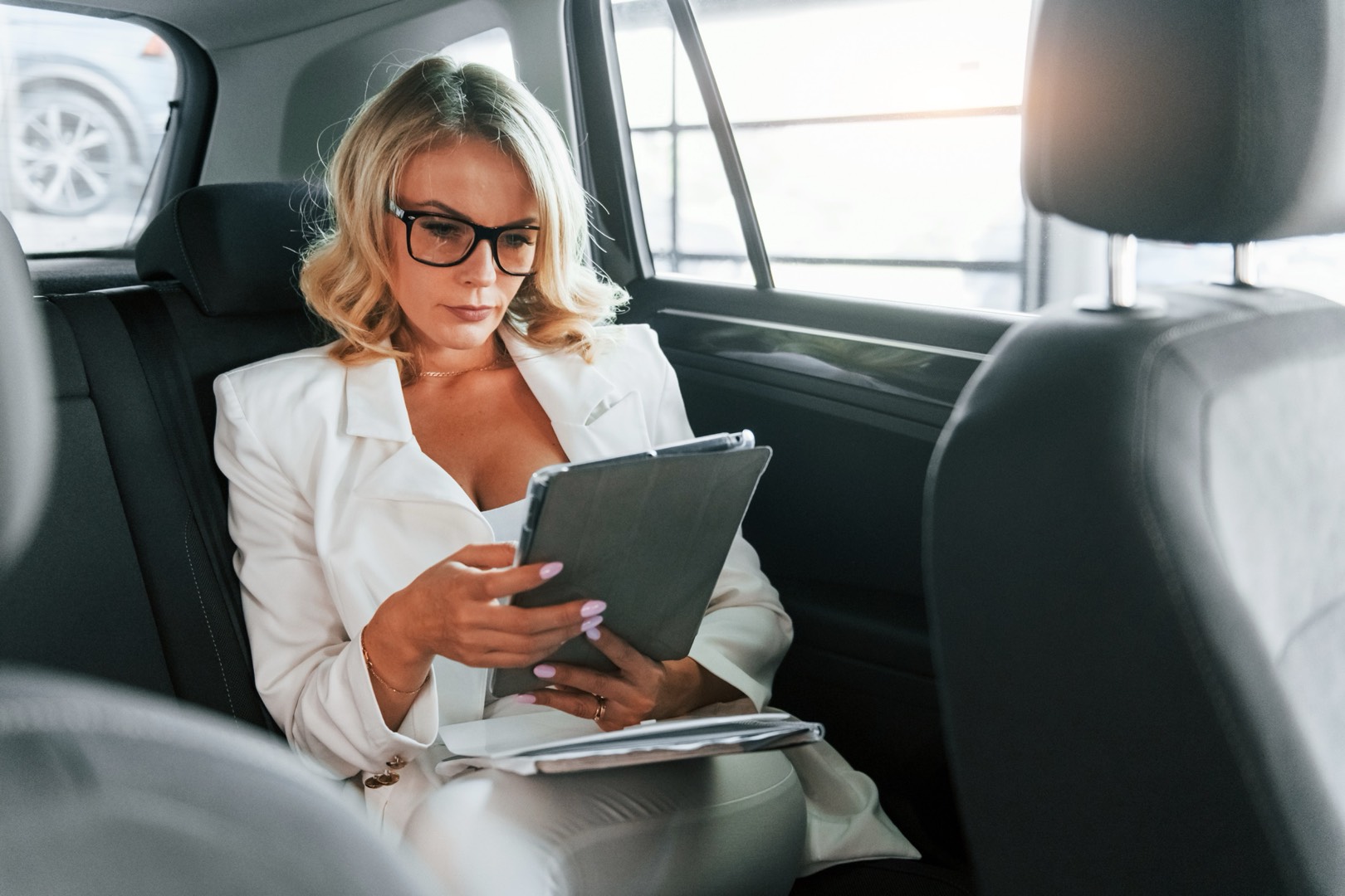 Donna in abito formale consulta comodamente un tablet mentre è seduta in auto