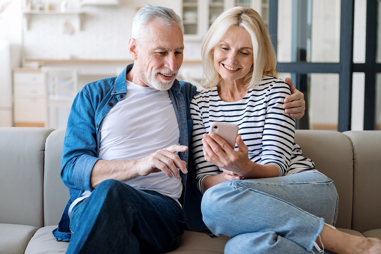 Coppia sorridente sul divano, guarda insieme una proposta di viaggio sullo smartphone