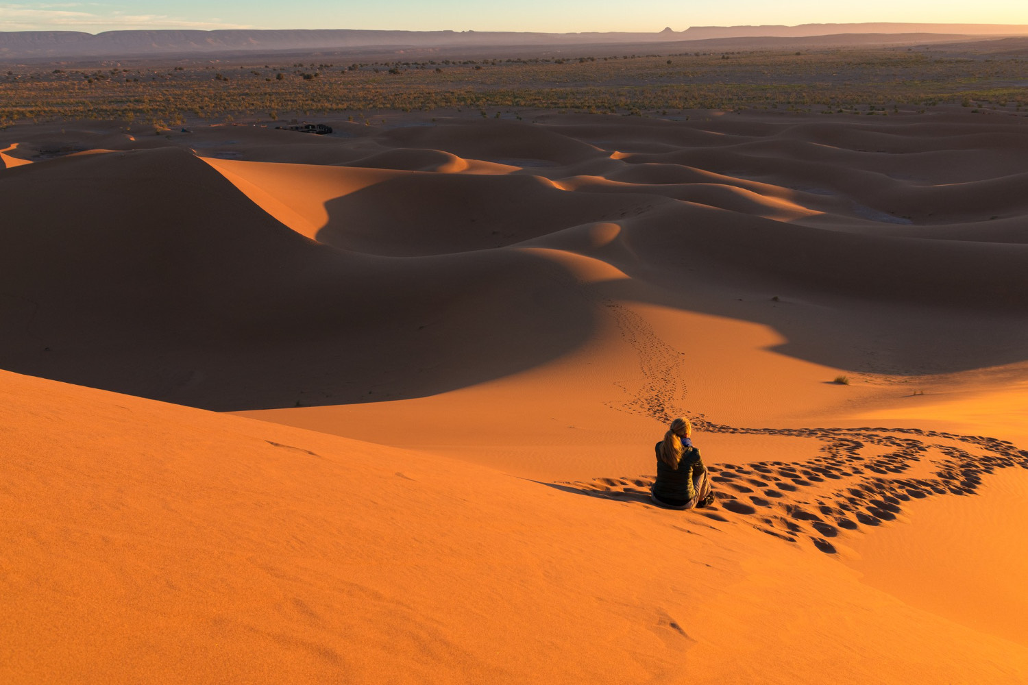 Viaggiatrice seduta in cima a una duna del deserto al tramonto