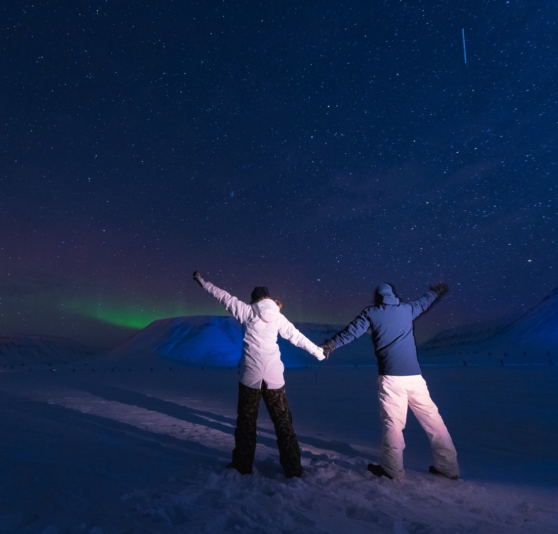 Coppia che ammira l'aurora boreale a braccia alzate nella notte innevata